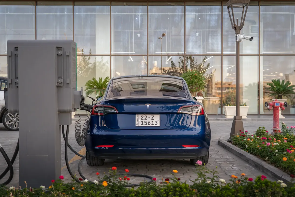 Rear view of a blue Tesla electric vehicle charging at a modern outdoor station.